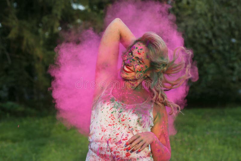 Portrait of happy young model having fun in a cloud of pink dry Holi paint at the park. Portrait of happy young woman having fun in a cloud of pink dry Holi royalty free stock image